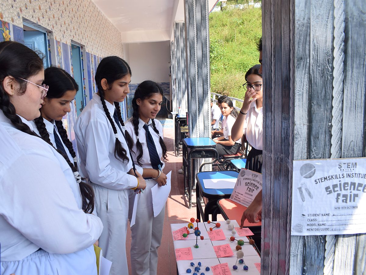 Students at the StemSkills science fair looking at ball-and-stick molecular models, beside a poster reading STEMSKILLS INSTITUTE science fair